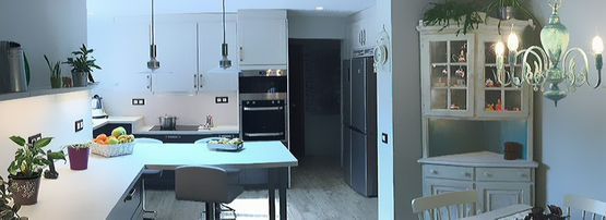 Una cocina con gabinetes blancos, electrodomésticos de acero inoxidable, una mesa y una lámpara de araña.