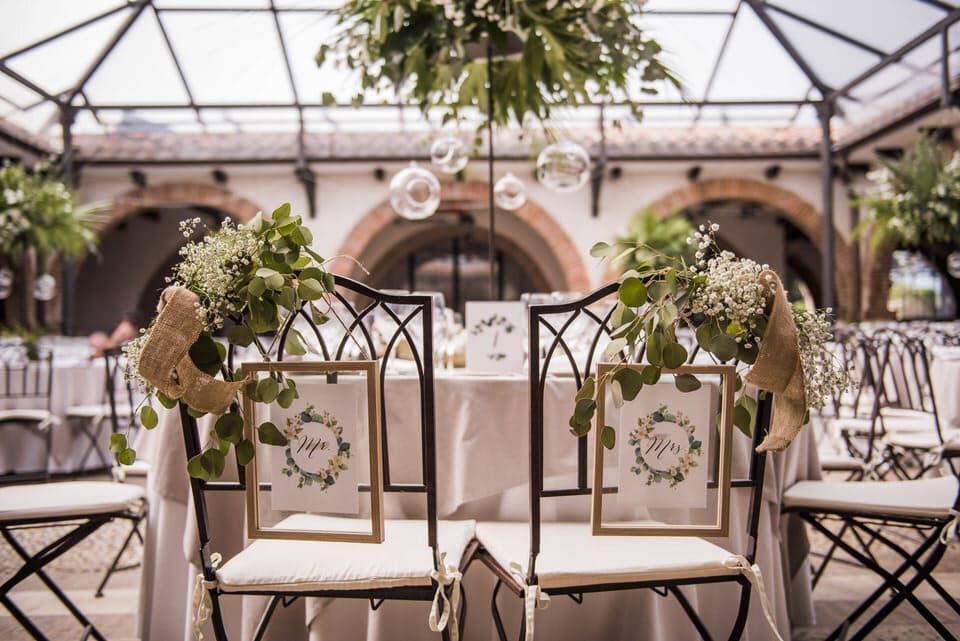 Recepción de boda al aire libre decorada, con sillas blancas, arreglos florales y lámparas de cristal colgantes en un patio