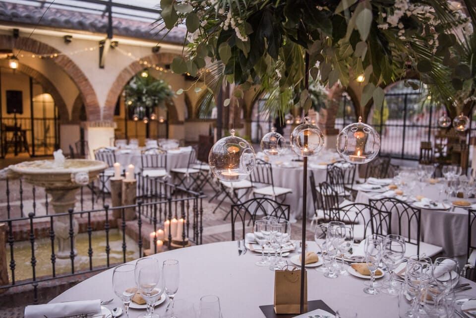 Elegante comedor en un patio con mesas redondas, manteles blancos y vegetación colgante bajo arcadas de piedra