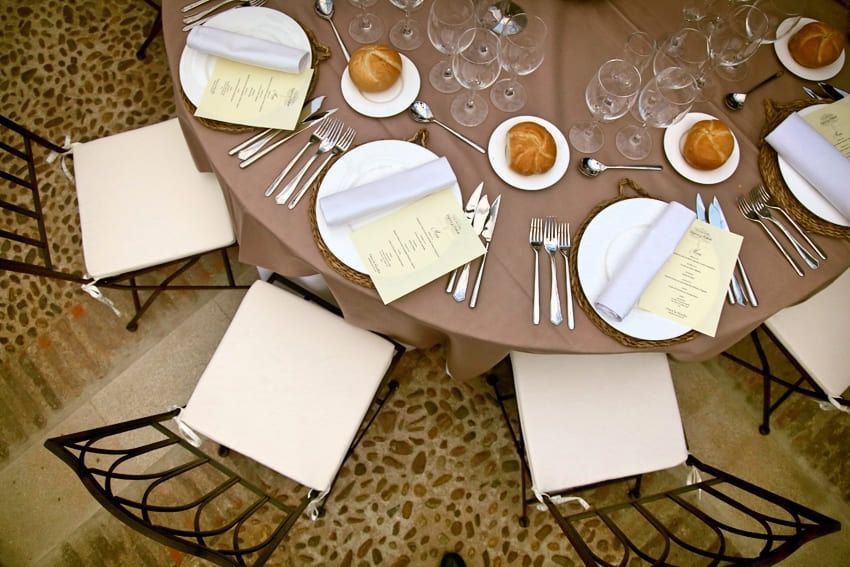 Mesa de comedor puesta con platos blancos, servilletas dobladas y cuencos naranjas sobre una alfombra estampada