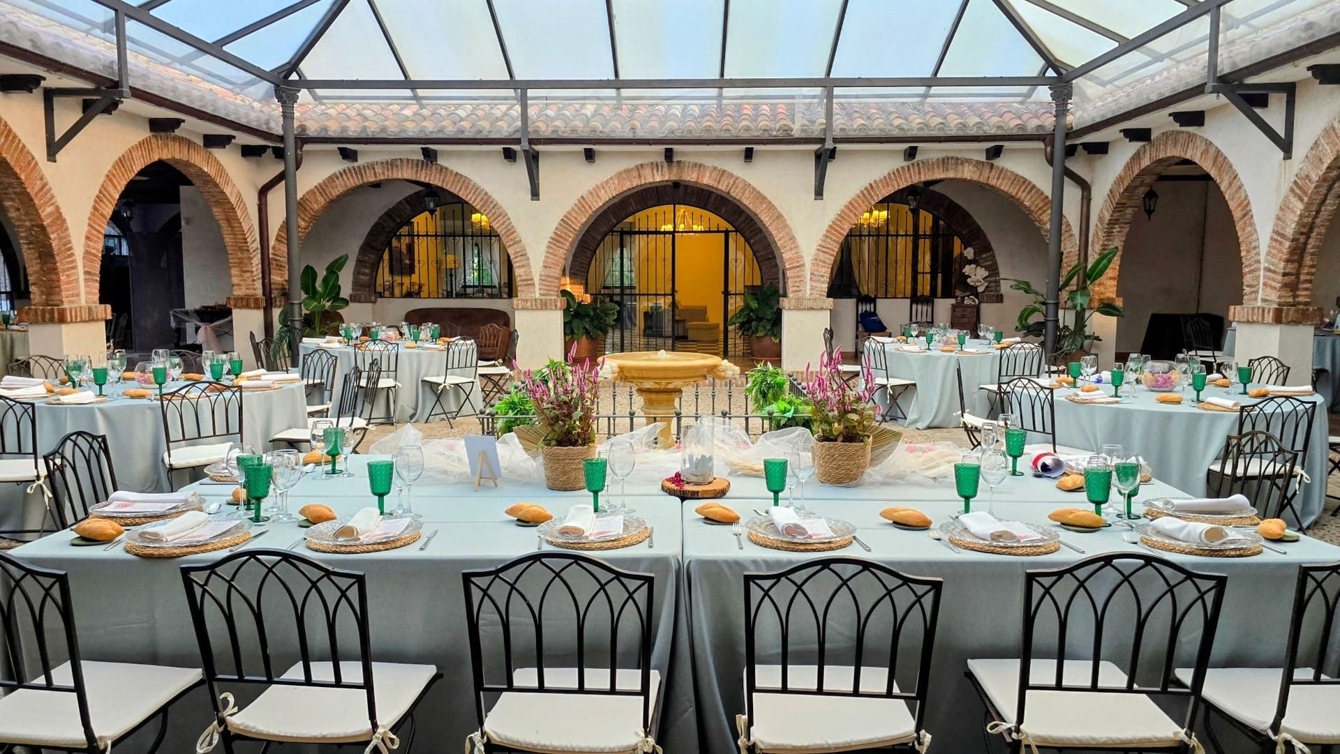 Elegante comedor en un patio con mesas redondas cubiertas con manteles blancos, sillas negras y arcos bajo un techo de cristal