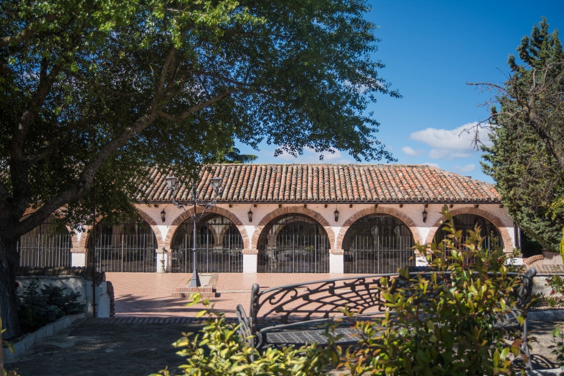 Patio con una columnata de arcos, tejado de tejas y árboles bajo un cielo azul despejado