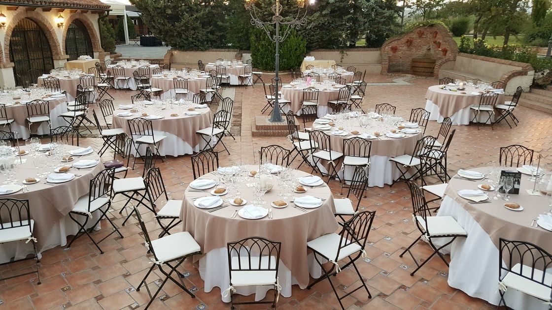 Comedor al aire libre con mesas redondas preparadas para un banquete en un patio de terracota