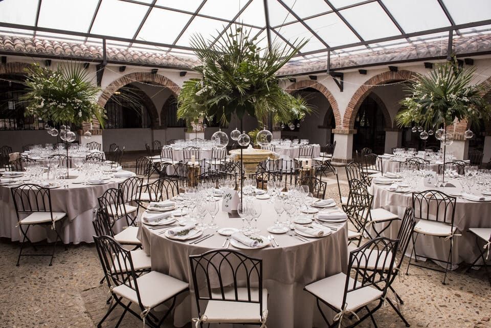 Elegante montaje de banquete en un patio, con mesas redondas cubiertas con manteles blancos y sillas bajo una cubierta de cristal.