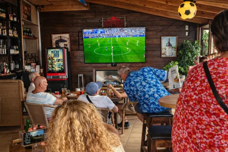 La gente se reúne en un bar rústico con paredes de madera para ver un partido de fútbol en una gran pantalla
