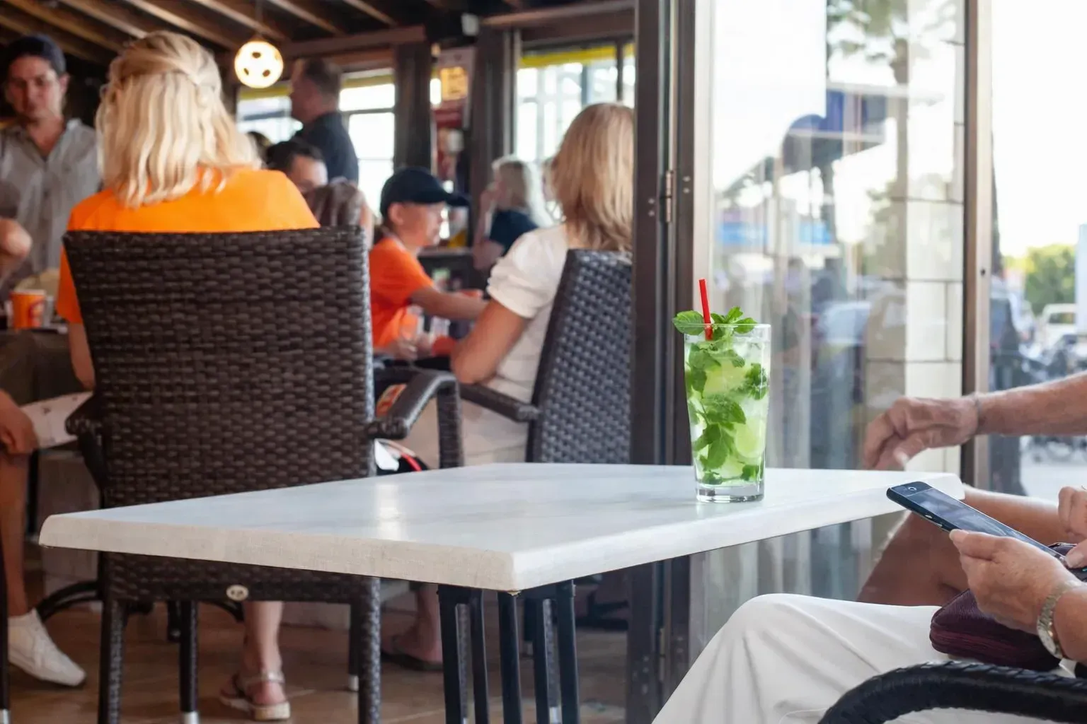 Varias personas están sentadas en mesas en la terraza de un restaurante al aire libre, con un cóctel verde