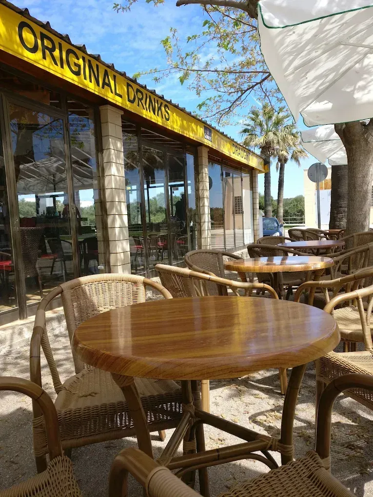 Patio al aire libre con mesas redondas de madera y sillas de mimbre en una cafetería