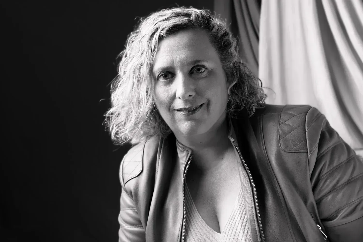 Retrato en blanco y negro de una persona inclinada hacia adelante, con una chaqueta de cuero y una leve sonrisa.