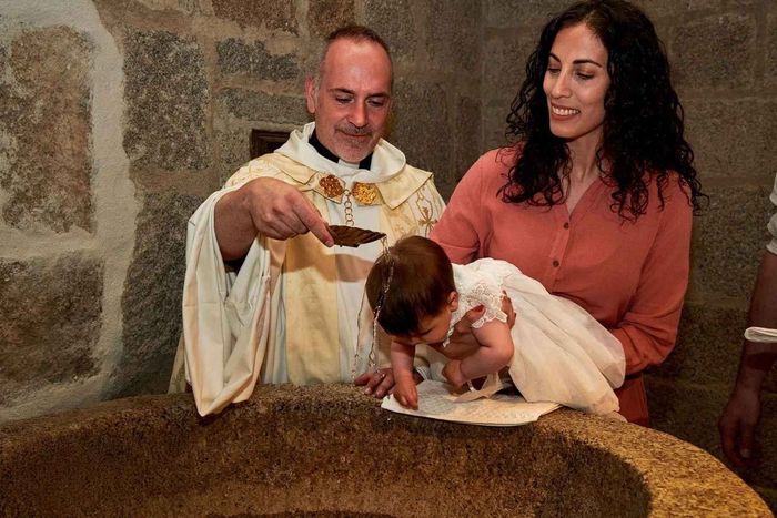 Ceremonia de bautismo en la que un sacerdote vierte agua sobre un bebé mientras una mujer sostiene al niño sobre una pila bautismal.