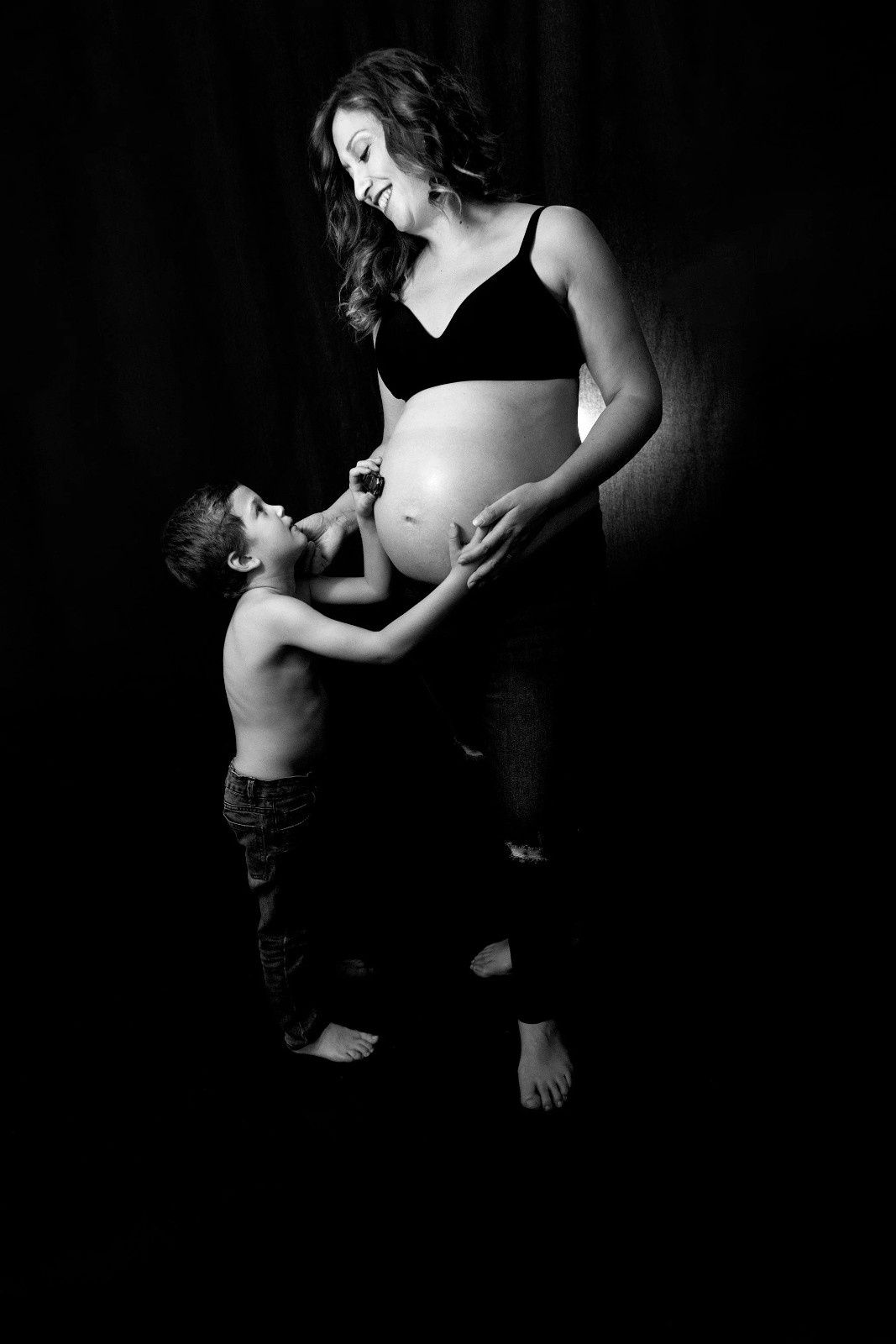 Fotografía en blanco y negro de una mujer embarazada sonriendo mientras un niño le toca la barriga.