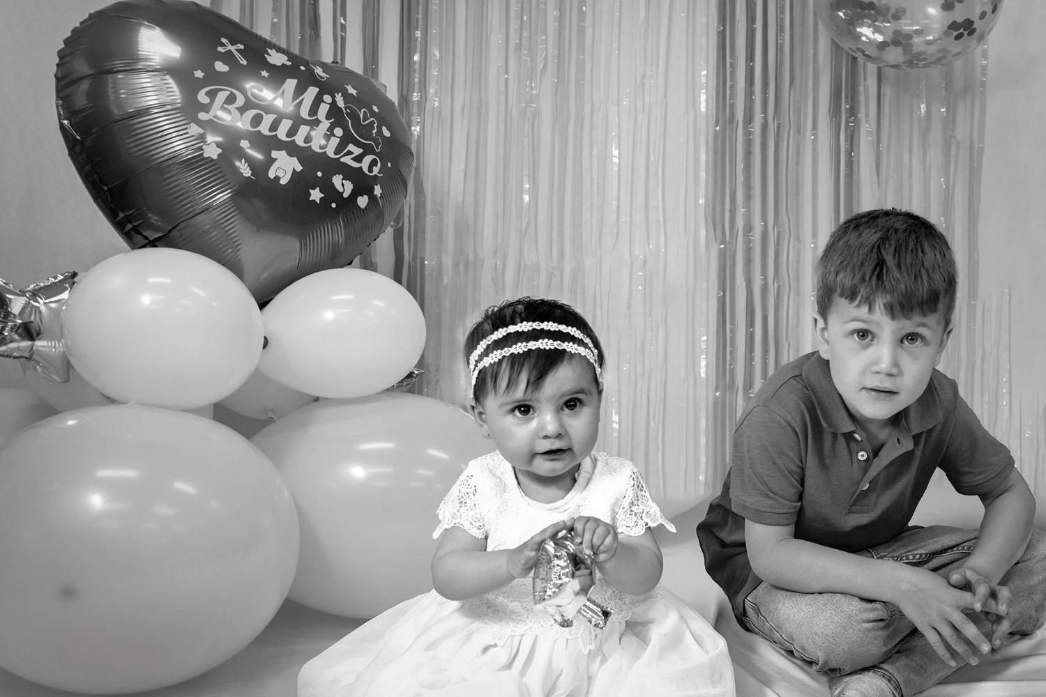 Dos niños sentados junto a globos en el fondo de una fiesta de cumpleaños.
