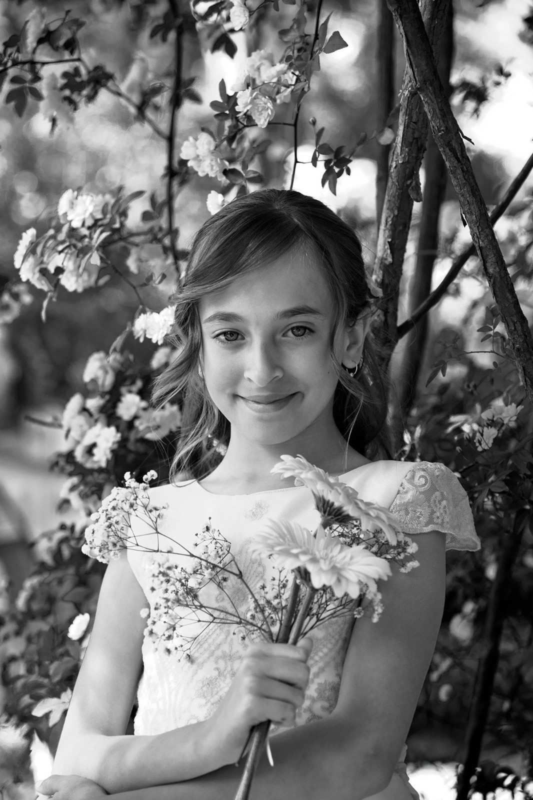Un niño sonriente sostiene un ramo de flores al aire libre junto a un árbol.