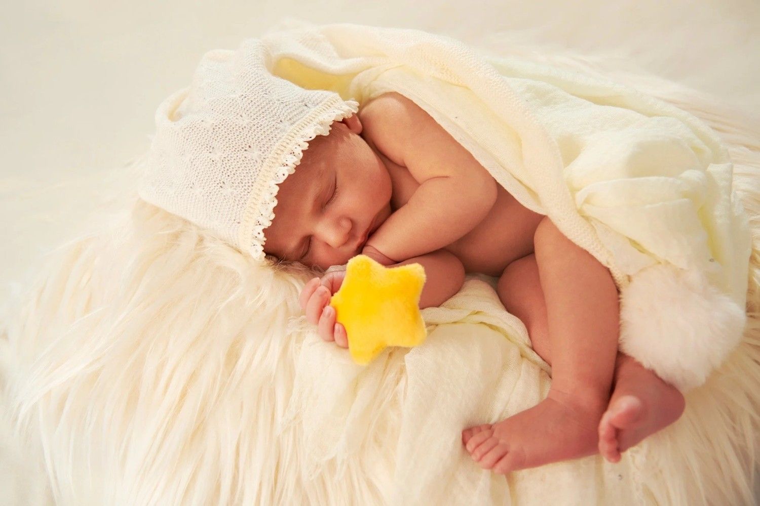Un bebé durmiendo sobre una suave manta blanca, sosteniendo un juguete con forma de estrella amarilla.
