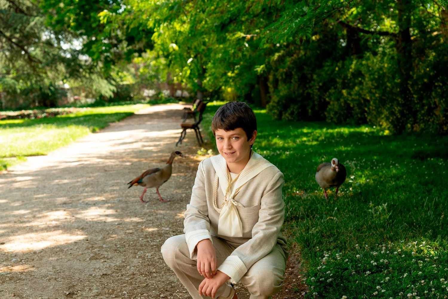 Persona agachada en un sendero de un parque junto a pájaros en un parque verde y soleado.