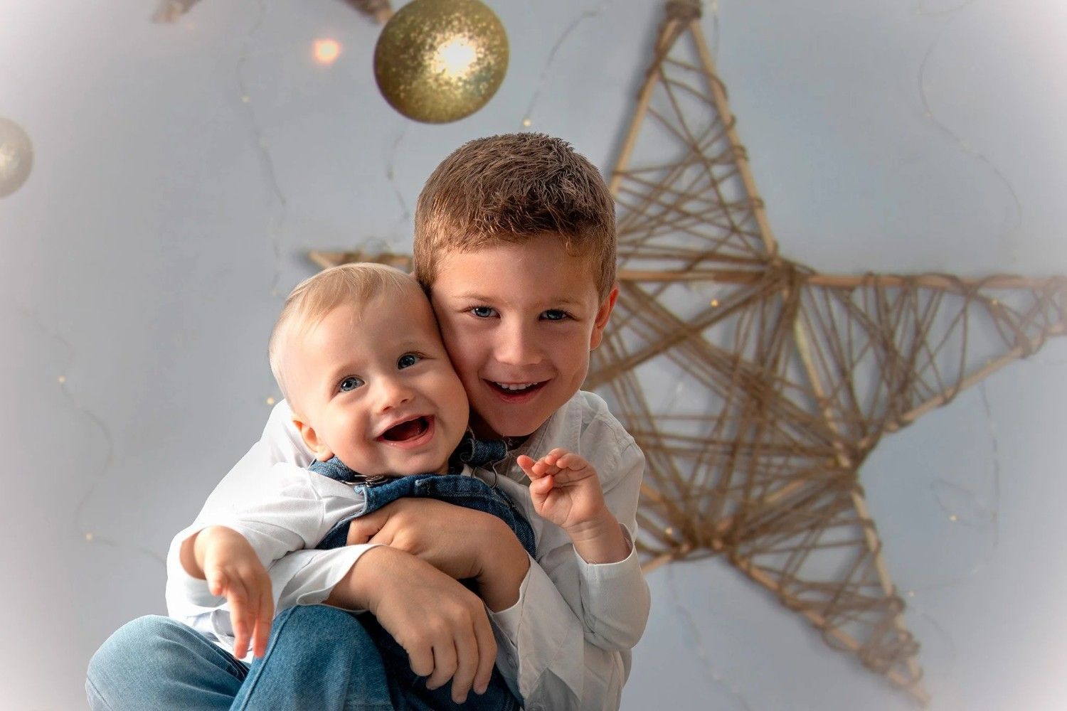 Dos niños sonrientes se abrazan frente a una gran estrella decorativa y adornos colgantes.