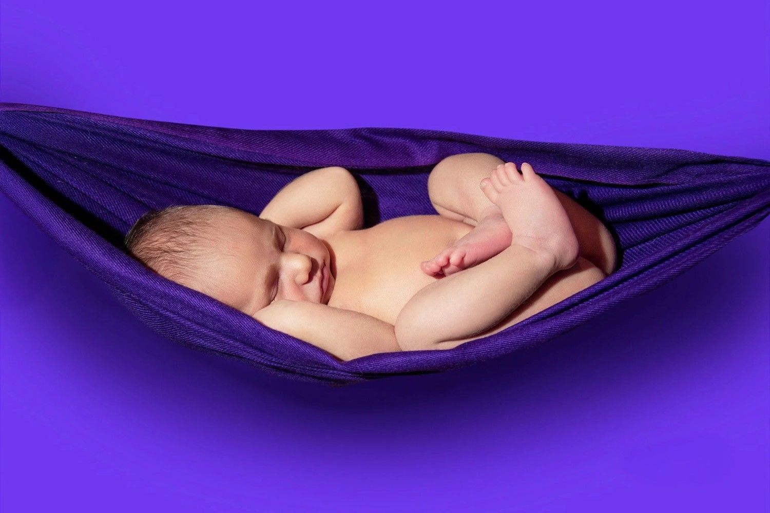 Bebé durmiendo en una hamaca morada sobre un fondo morado.