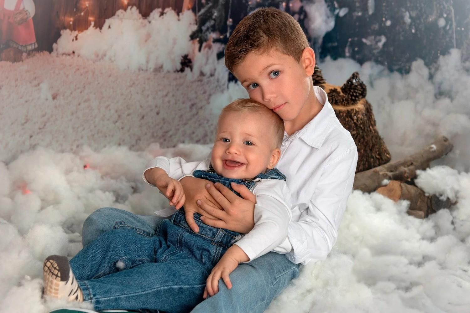 Dos niños sentados juntos en una mullida escena invernal blanca, sonriendo y acurrucándose bajo suaves mantas.
