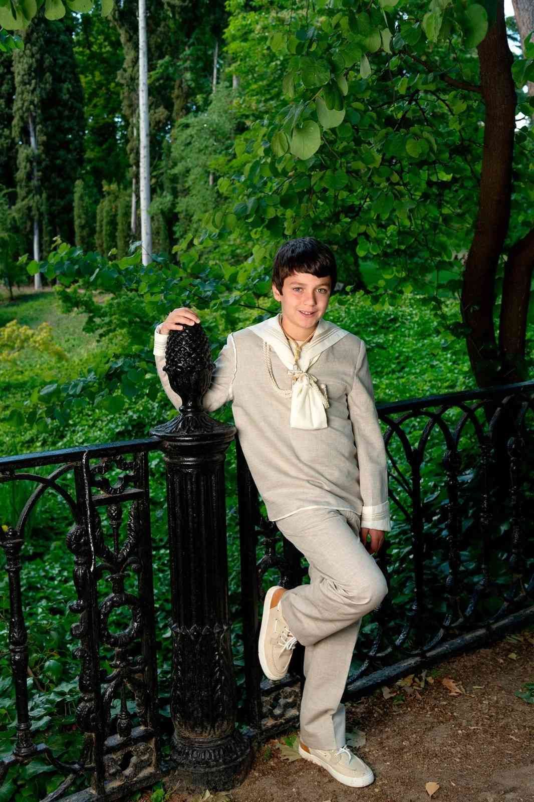 Persona vestida de color beige apoyada en una barandilla negra en un parque de exuberante vegetación.