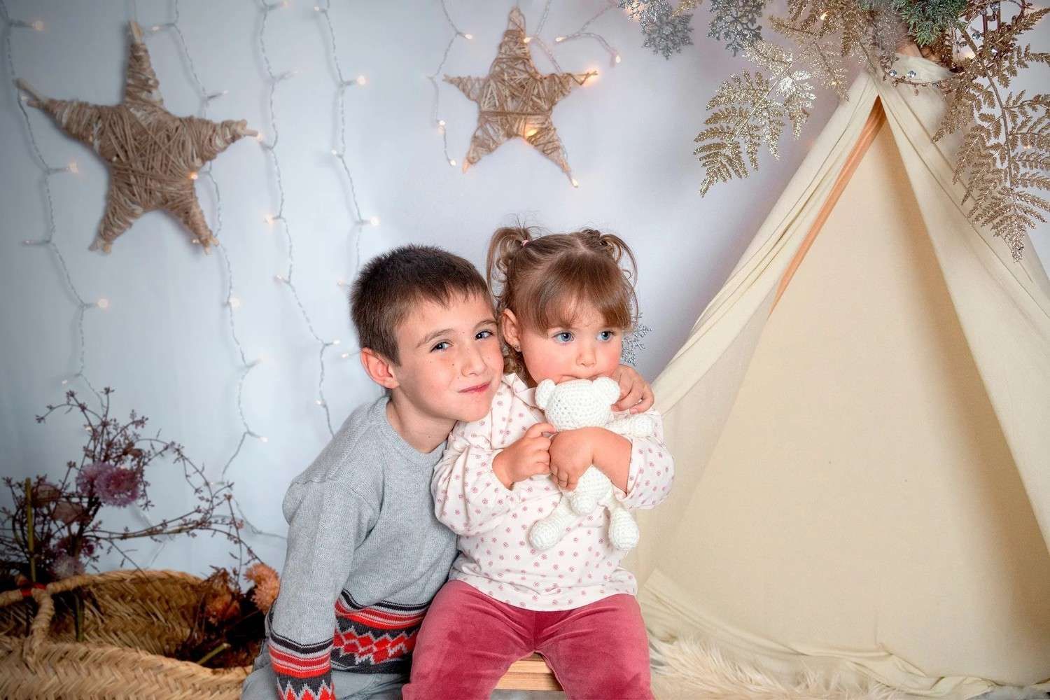 Dos niños sentados junto a un tipi beige con decoraciones de estrellas doradas, uno abrazando al otro.