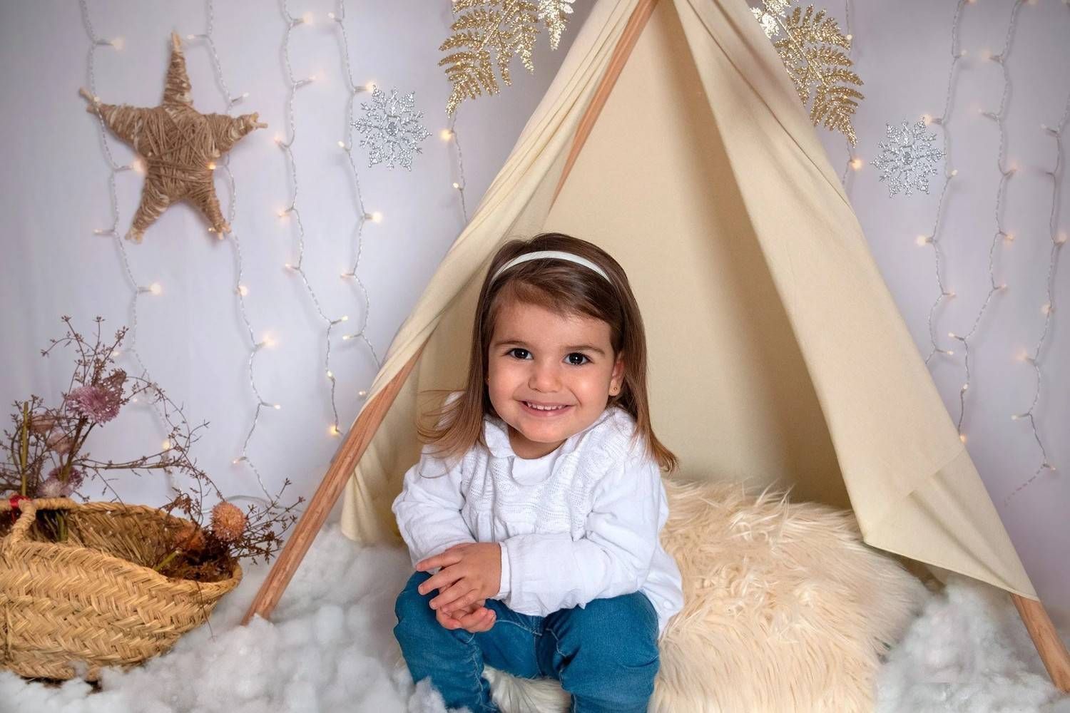 Niña sonriente dentro de un tipi color crema con decoraciones de estrellas blancas y acogedoras mantas de piel sintética.