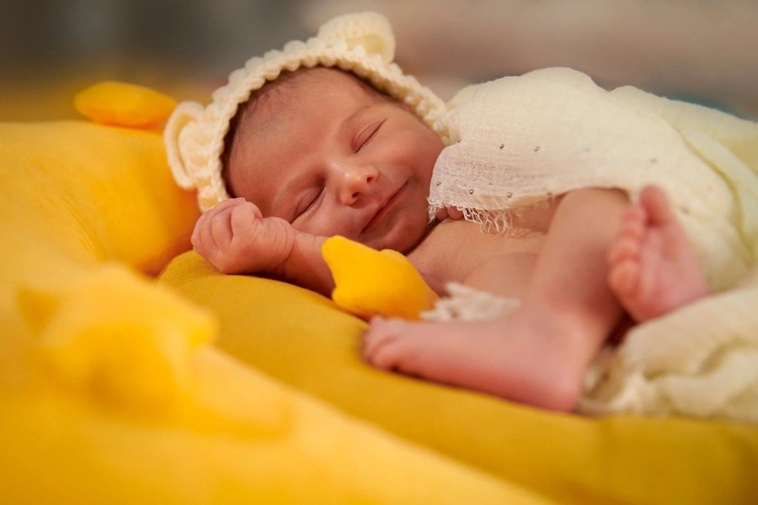 Bebé durmiendo sobre una suave manta amarilla con un gorro de punto blanco y un conjunto de encaje.