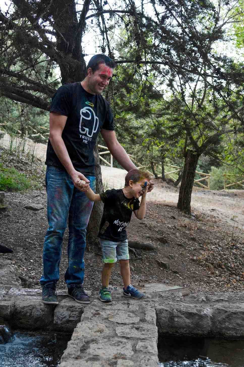 Un adulto y un niño están de pie en un sendero de piedra junto al agua, tomados de la mano en un parque arbolado.