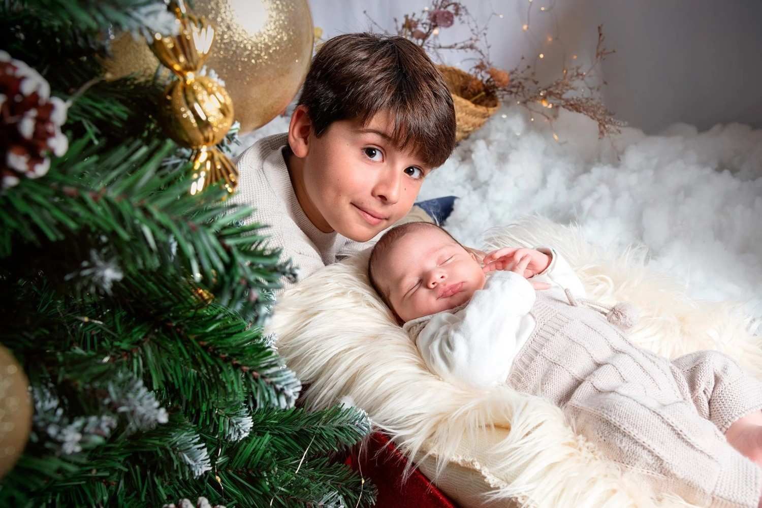 Dos niños acurrucados en una acogedora escena navideña junto a un árbol de Navidad decorado.