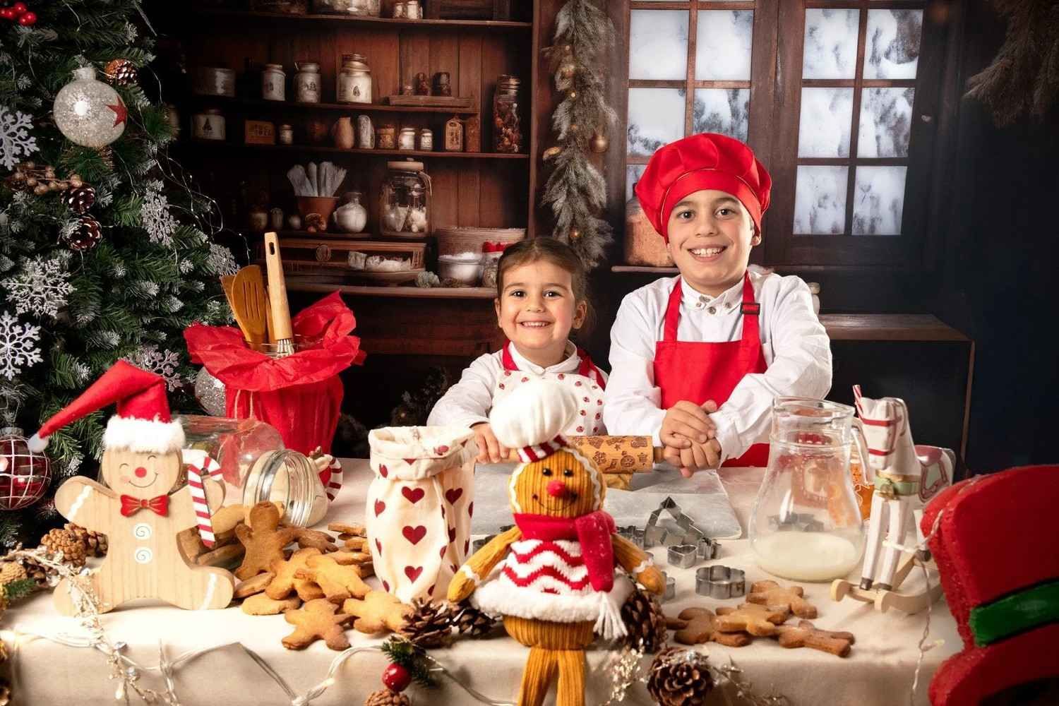 Dos niños con delantales rojos y blancos horneando en una mesa festiva con galletas y adornos navideños.
