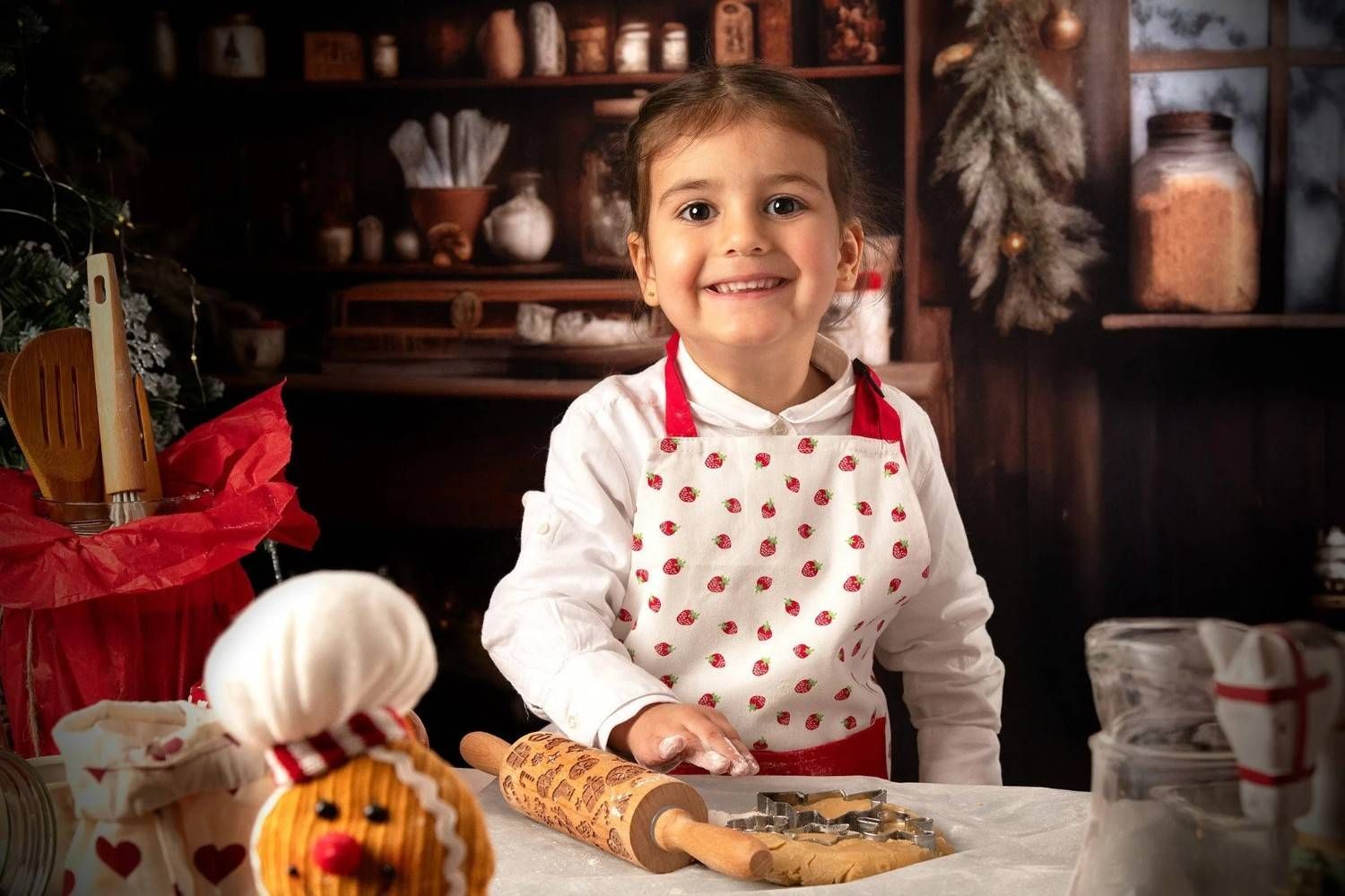 Una niña con un delantal blanco de lunares sonríe mientras amasa en una acogedora cocina.