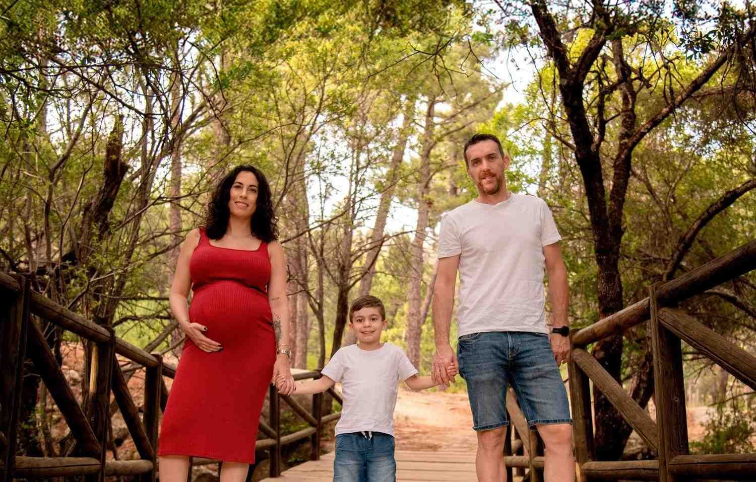 Una familia camina junta por un sendero boscoso; una mujer embarazada, un niño y un hombre van tomados de la mano.
