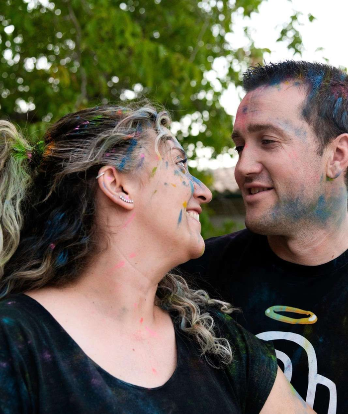 Dos personas sonriéndose mutuamente al aire libre, con la cara pintada y un fondo de hojas.