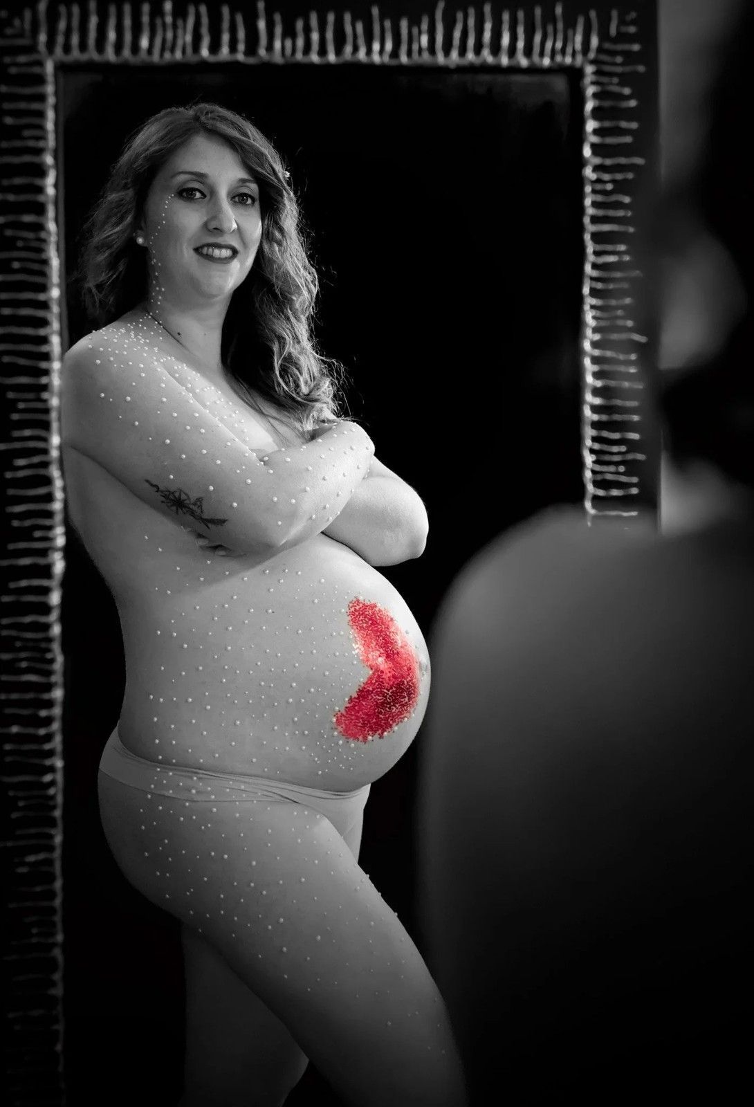 Mujer embarazada posando en blanco y negro, con el vientre pintado de rojo brillante sobre un fondo oscuro.
