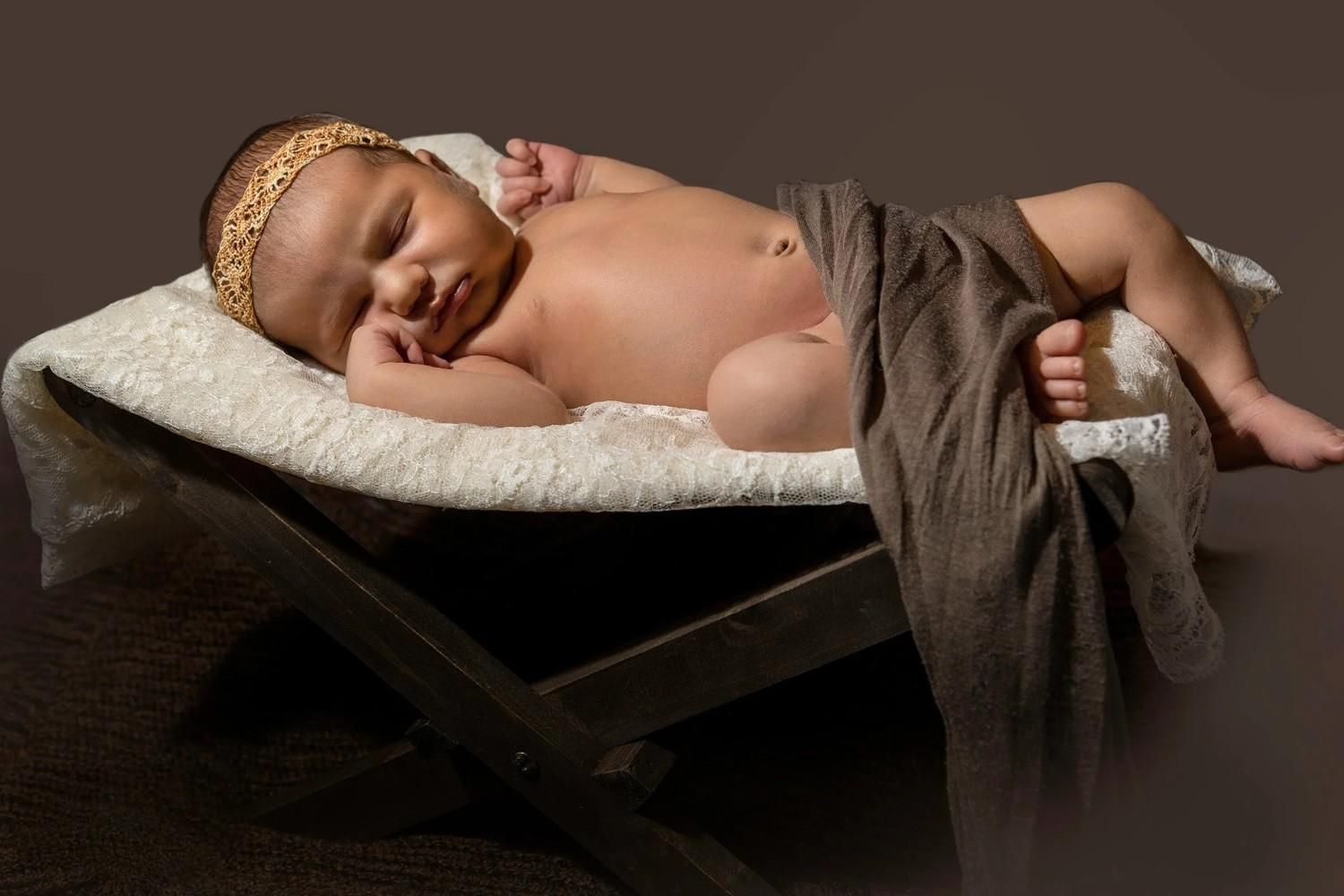 Un bebé durmiendo en un banco acolchado, con un gorrito de encaje y cubierto con una tela marrón.