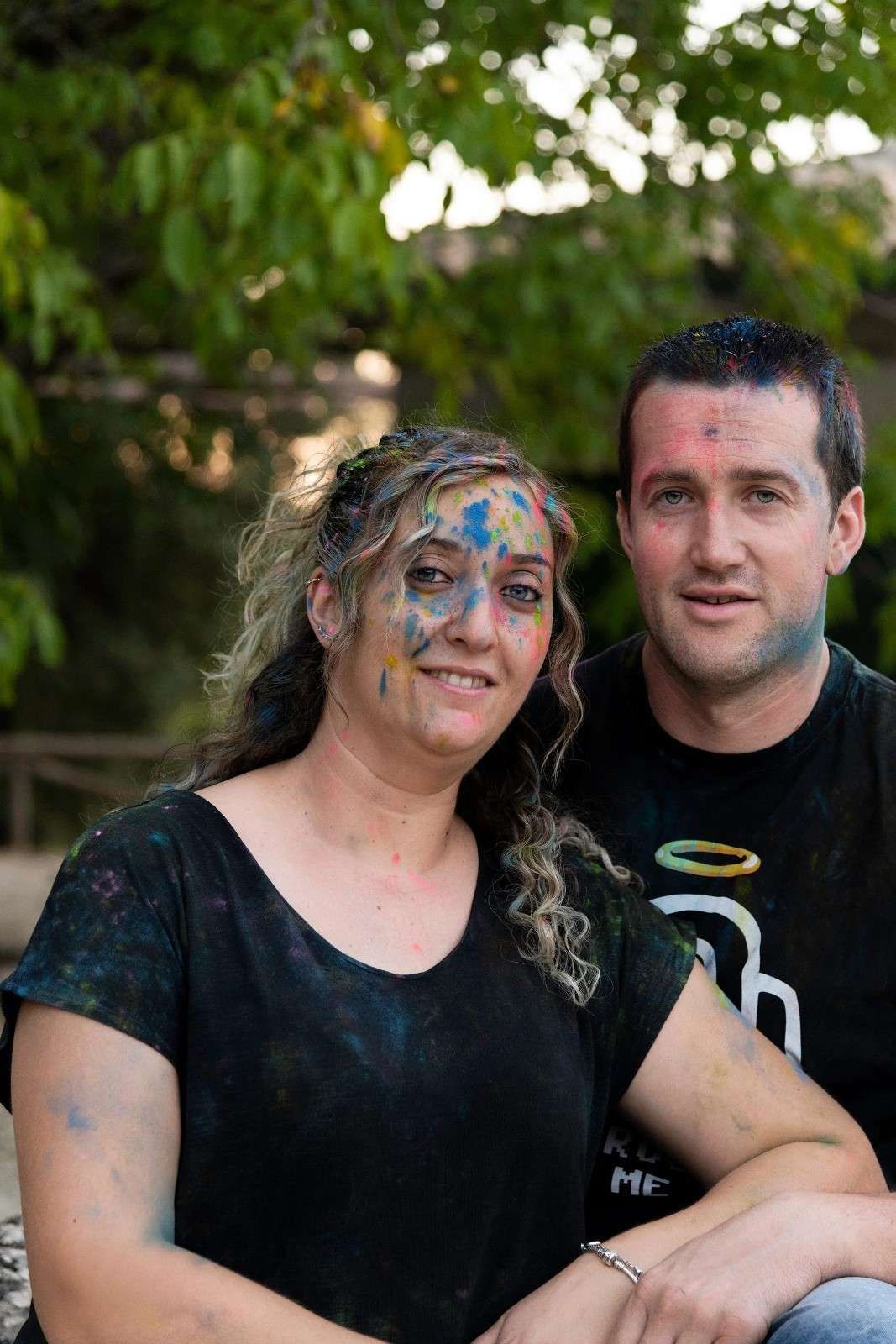 Dos personas de pie al aire libre, una con la cara pintada de azul y ambas con camisas oscuras.