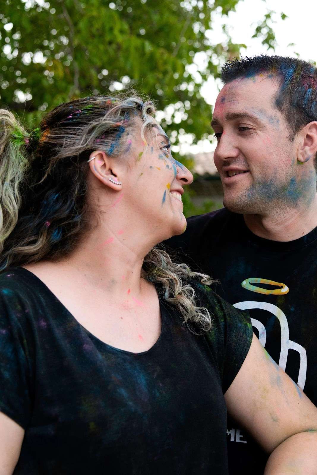 Dos personas sonrientes se miran fijamente al aire libre, vestidas con camisetas negras y con la cara pintada en las mejillas.