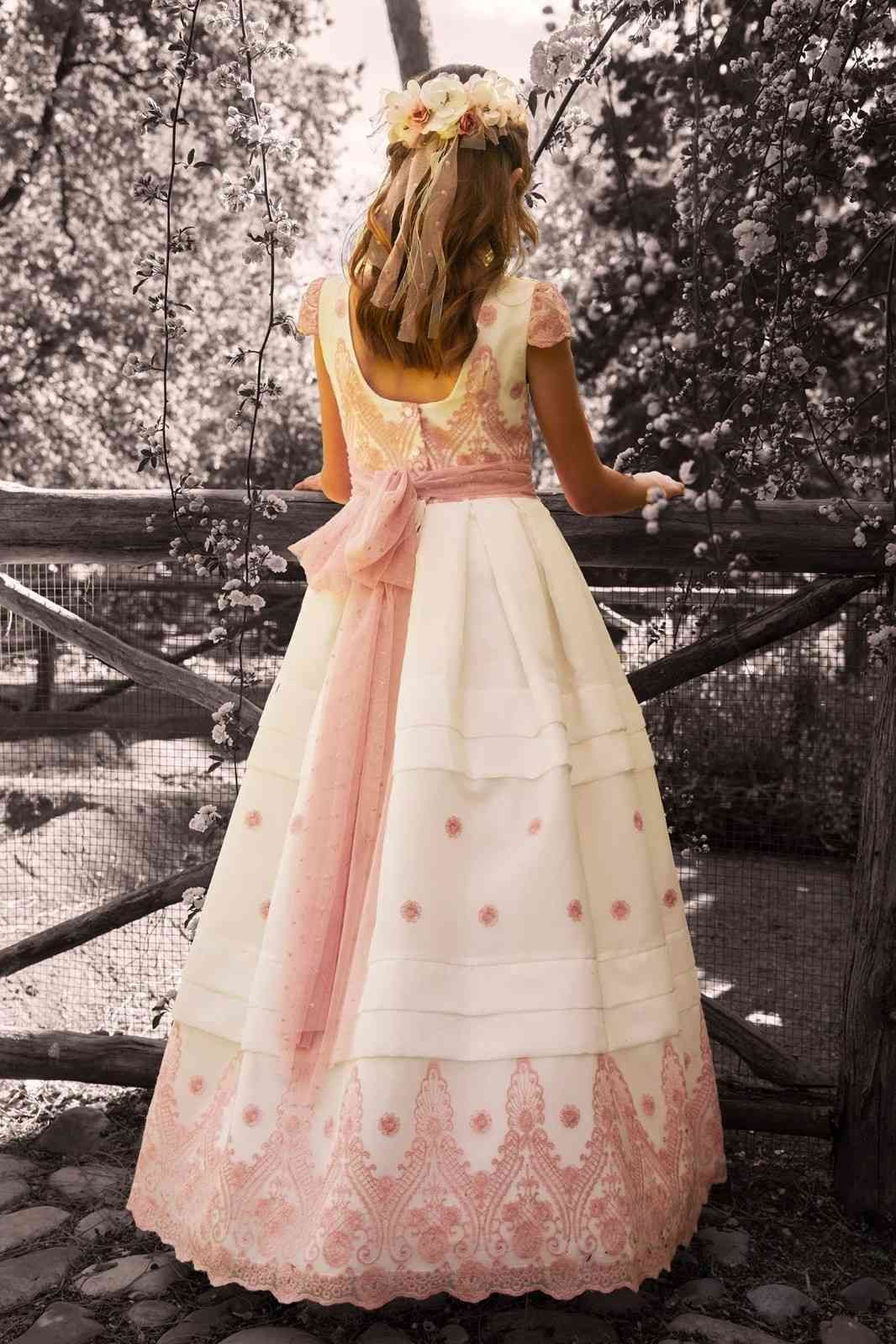 Una niña con un vestido rosa pastel está de pie sobre un puente en un jardín arbolado.