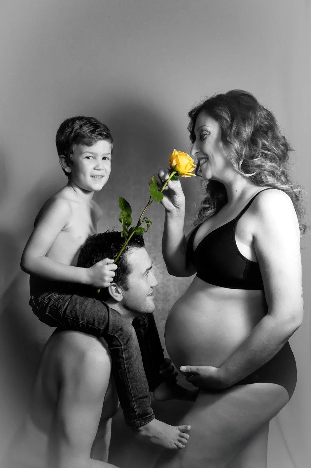 Retrato de maternidad en blanco y negro de dos niños interactuando con una mujer embarazada que sostiene una rosa amarilla.
