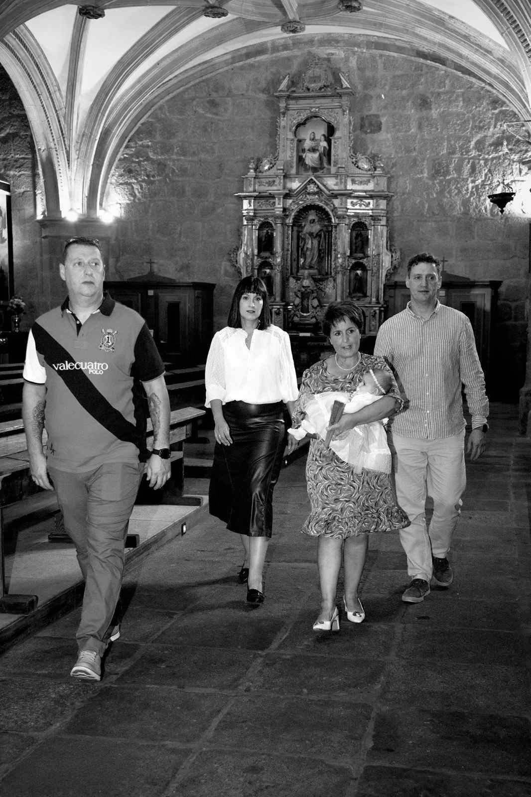 Cuatro personas caminan por el interior abovedado de una iglesia, con un altar ornamentado al fondo.