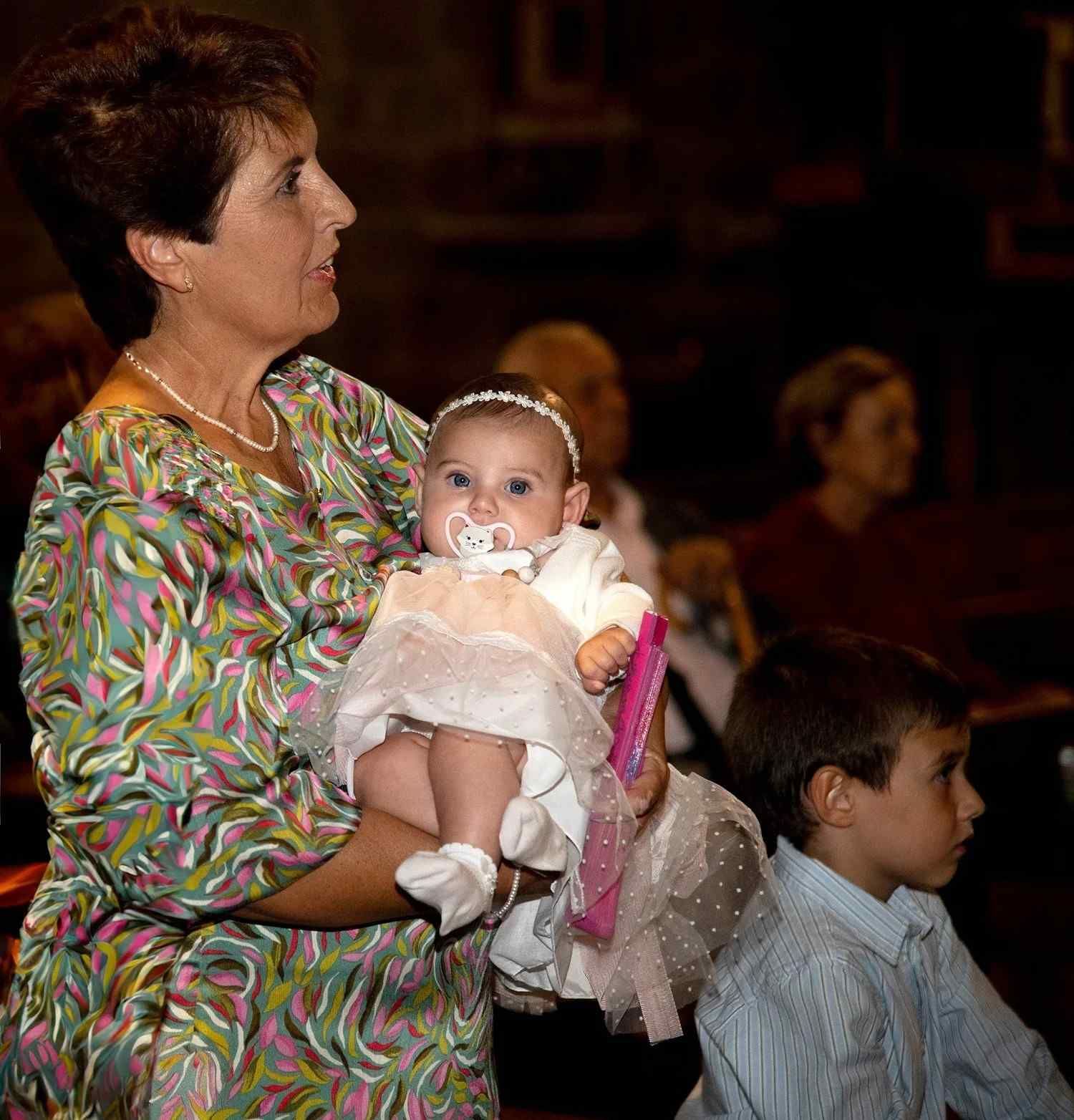 Mujer con un vestido rosa sosteniendo a un bebé en un evento formal en interiores.