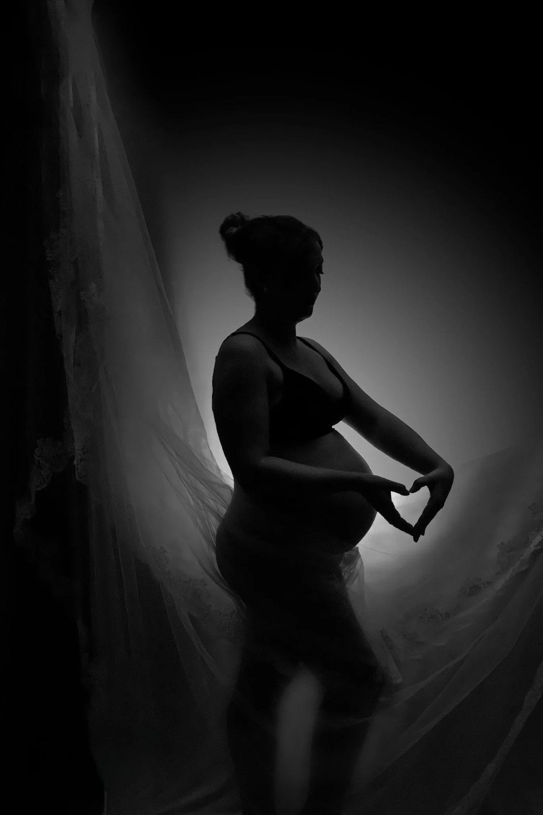 Bailarina en silueta posando bajo un dramático foco de luz en blanco y negro, con los brazos curvados hacia adelante.