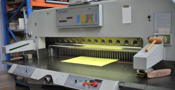 Une grande machine à découper le papier avec une feuille de papier jaune en position de découpe.