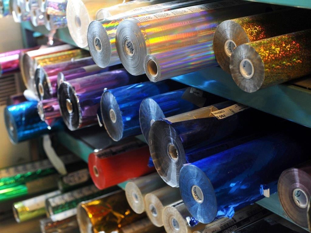 Des étagères contenant de nombreux rouleaux de papier aluminium coloré et métallisé pour l'impression ou les loisirs créatifs.