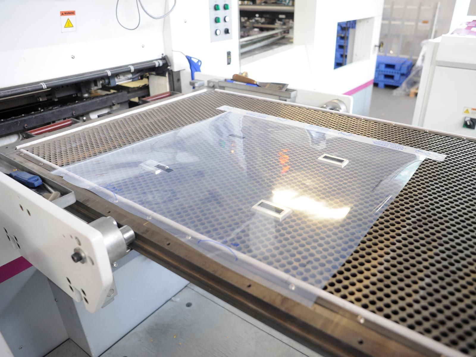 Une feuille de plastique transparent sur une surface métallique perforée à l'intérieur d'une machine de fabrication.