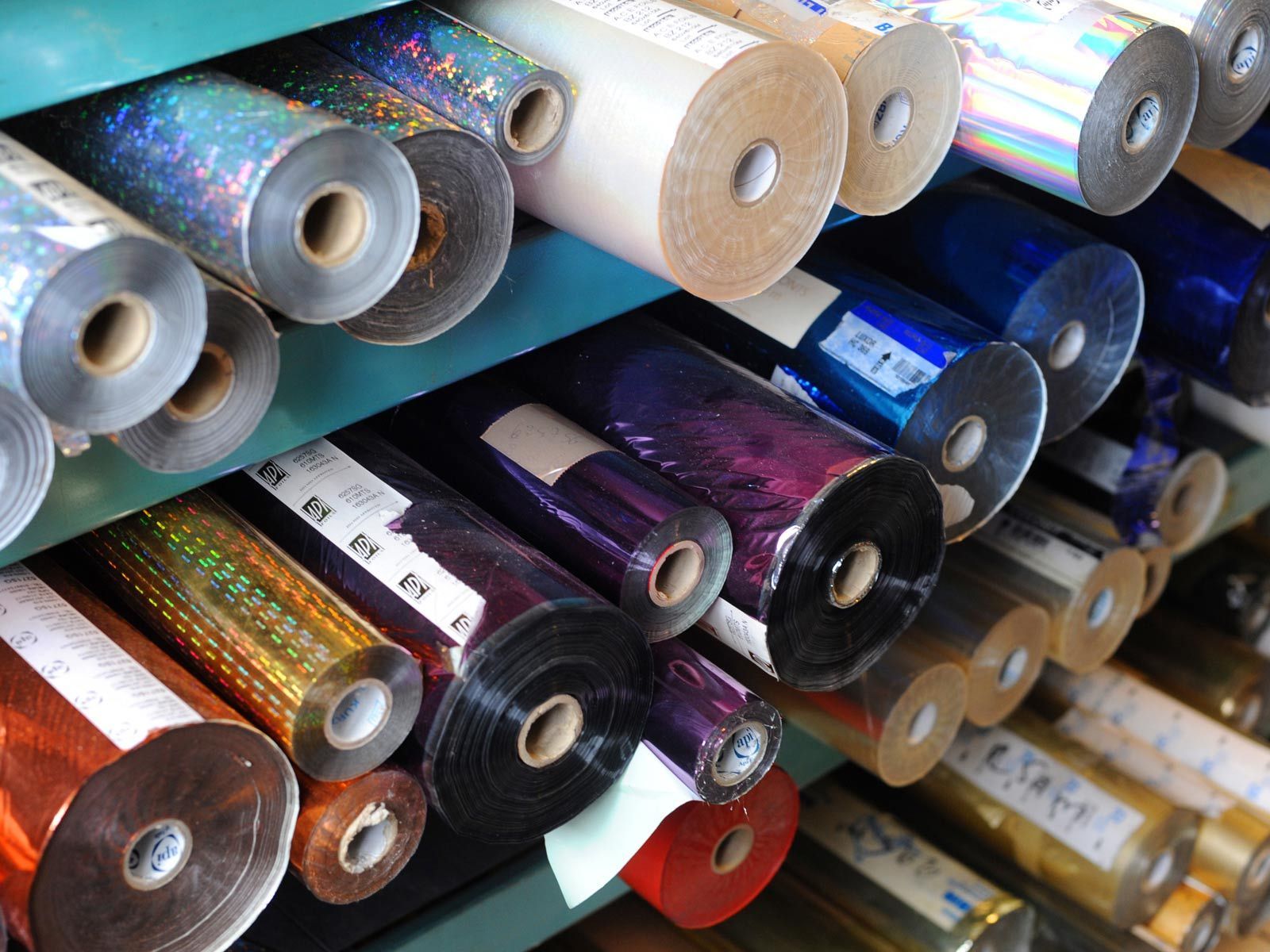 Des étagères remplies de rouleaux de papier aluminium brillant de différentes couleurs.