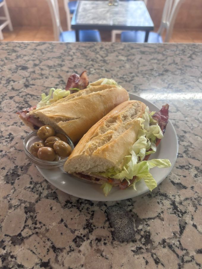 Dos sándwiches en un plato con aceitunas y lechuga rallada sobre una encimera moteada.