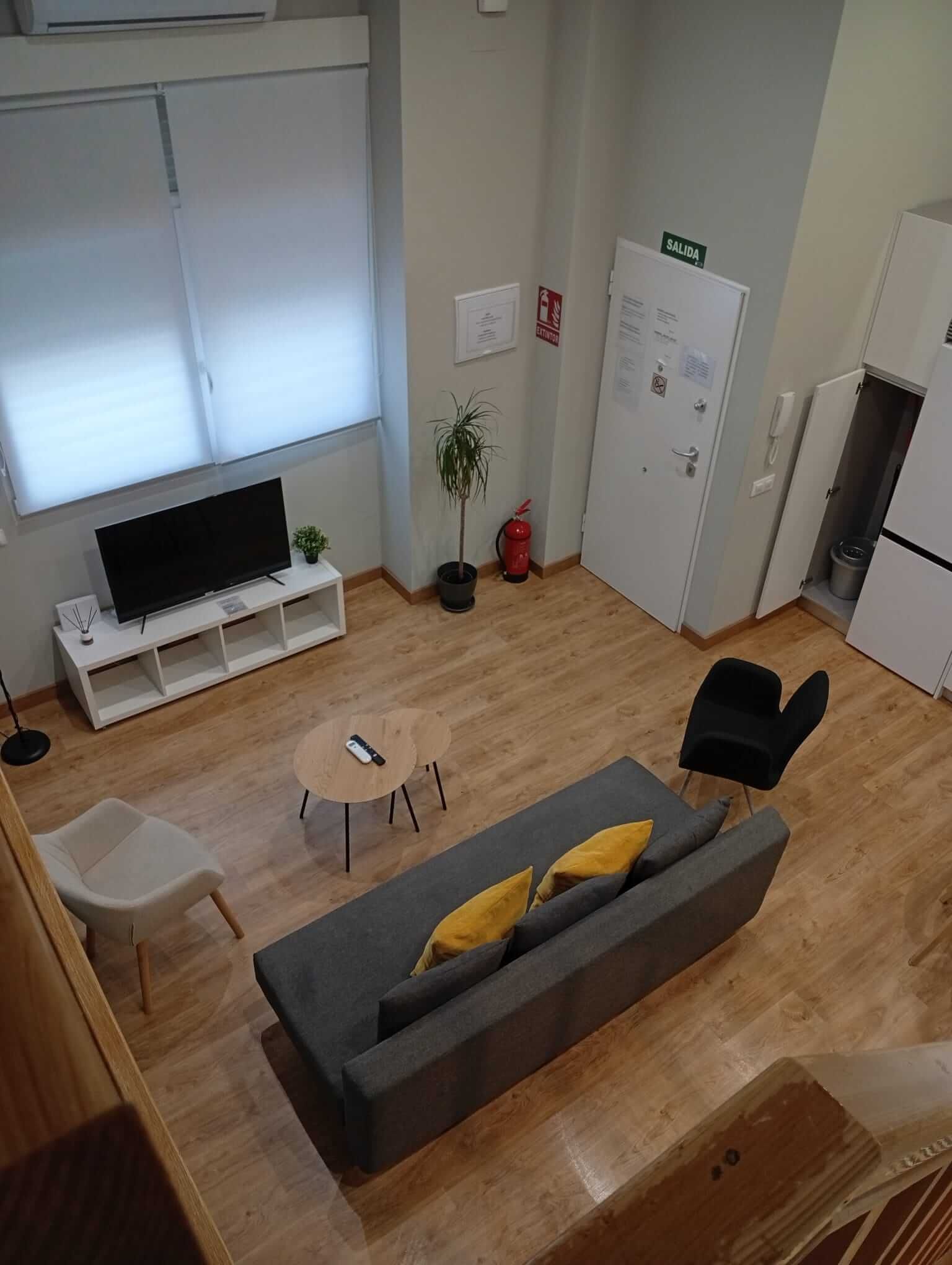 Sala de estar tipo loft con sofá gris, televisor, sillón y mesa de centro redonda sobre suelo de madera.