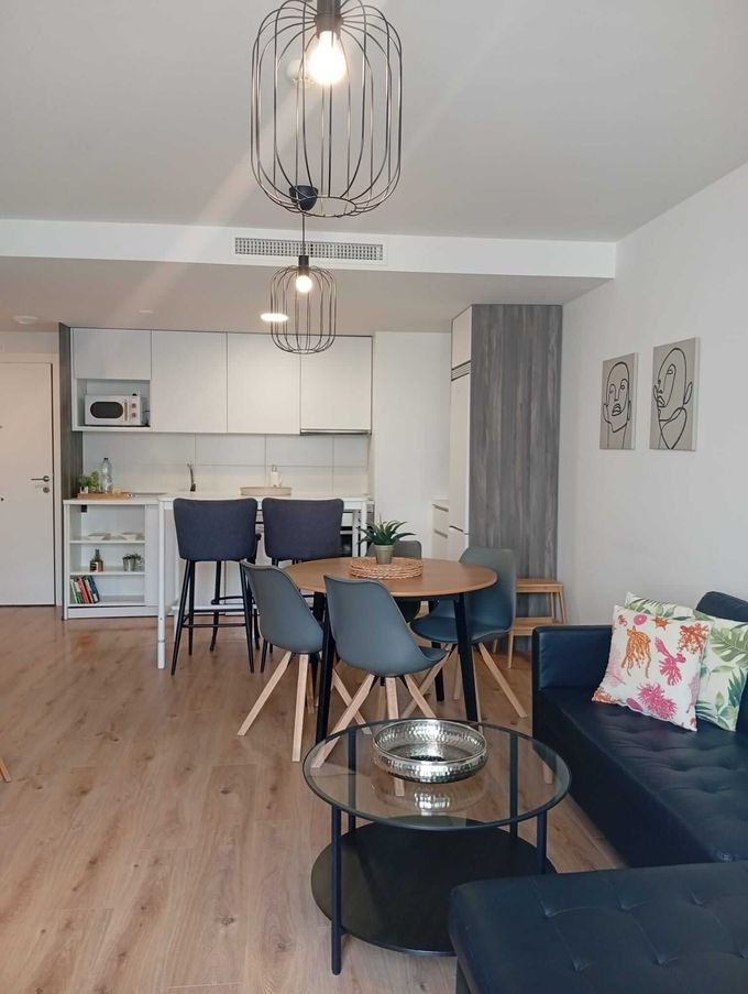 Salón-cocina moderno de planta abierta con sofá azul, mesa redonda y suelos de madera clara.