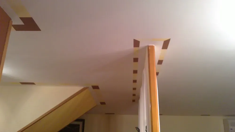 Techo con vigas y molduras de madera. Paredes y escaleras beige. Pequeñas piezas rectangulares marrones se fijan al techo