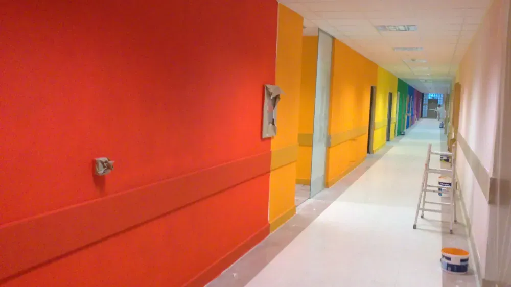 Pasillo de hospital con paredes pintadas con colores del arco iris, con una escalera al final.