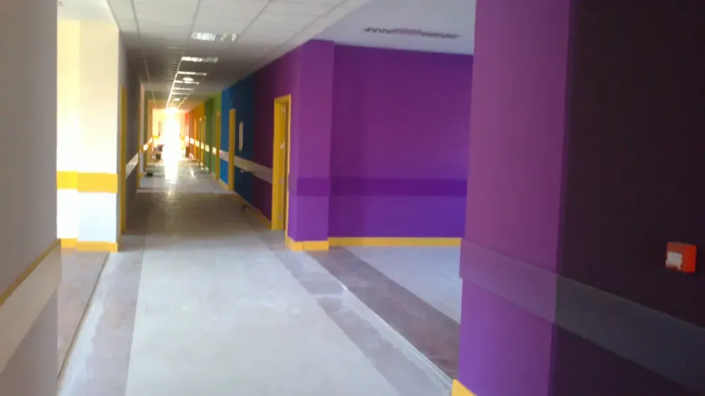 Pasillo de hospital con paredes de color violeta, azul y amarillo, suelo de baldosas y puertas.